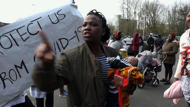 Eine Frau steht vor einem Plakat mit der Aufschrift "Protect us from Covid-19"